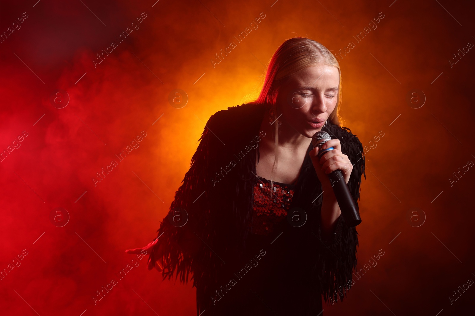 Photo of Beautiful singer performing on dark background with red light and smoke. Space for text