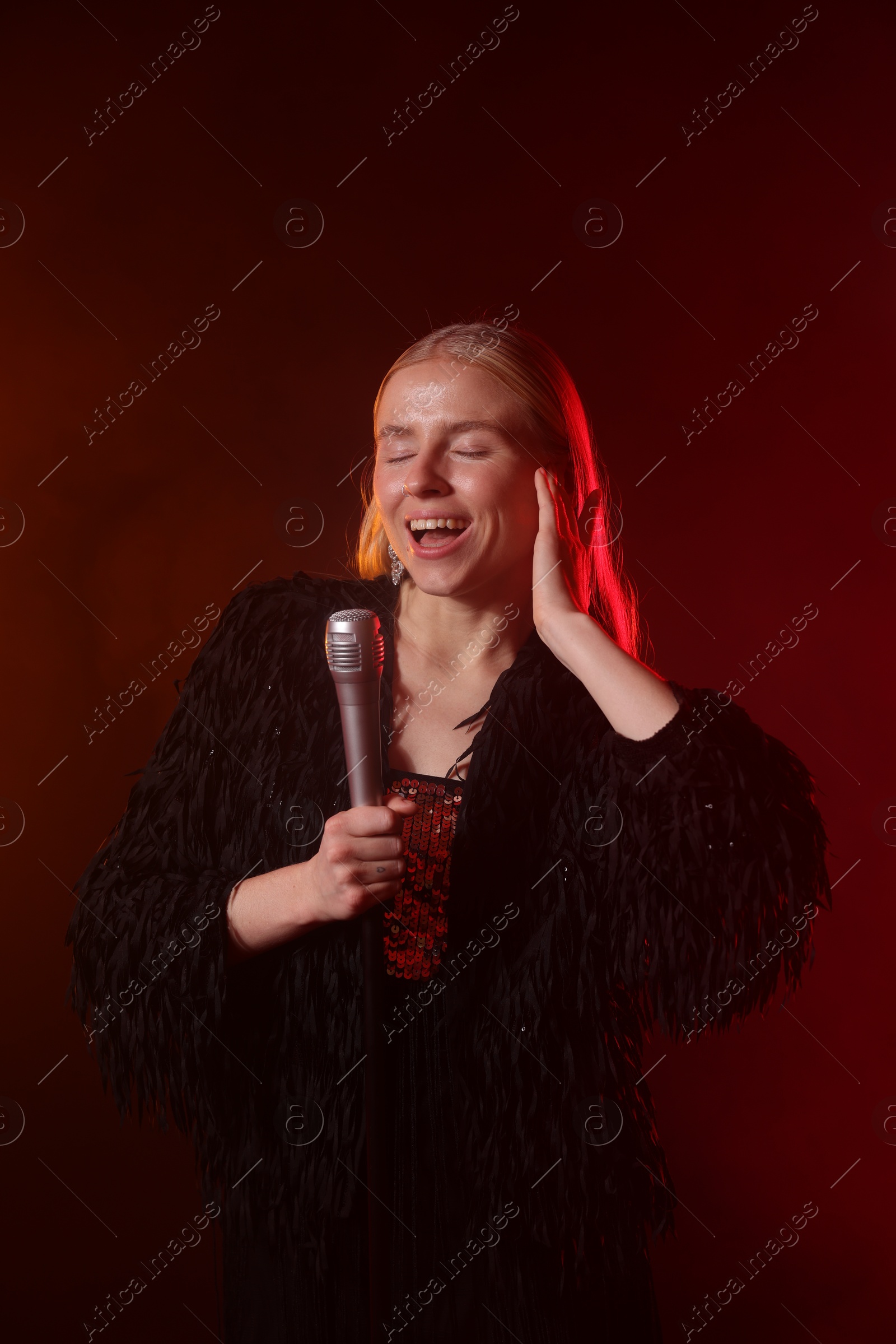 Photo of Beautiful singer performing on dark background with red light