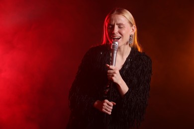 Beautiful singer performing on dark background with red light and smoke. Space for text