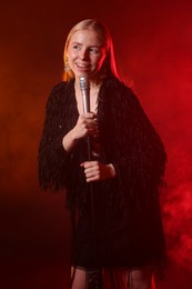 Beautiful singer performing on dark background with red light and smoke