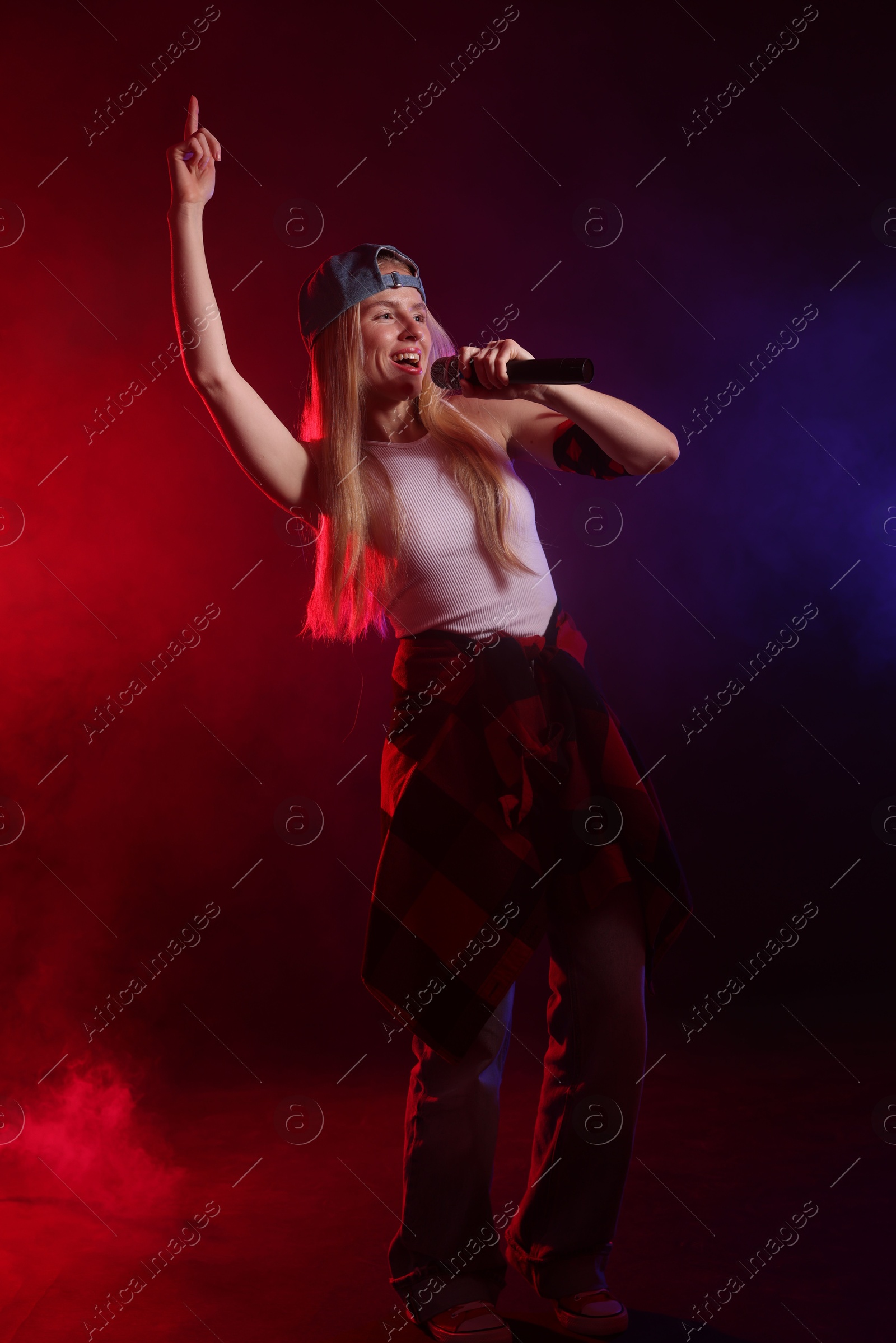 Photo of Talented singer performing on dark background with color lights and smoke