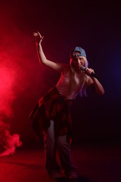 Photo of Talented singer performing on dark background with color lights and smoke