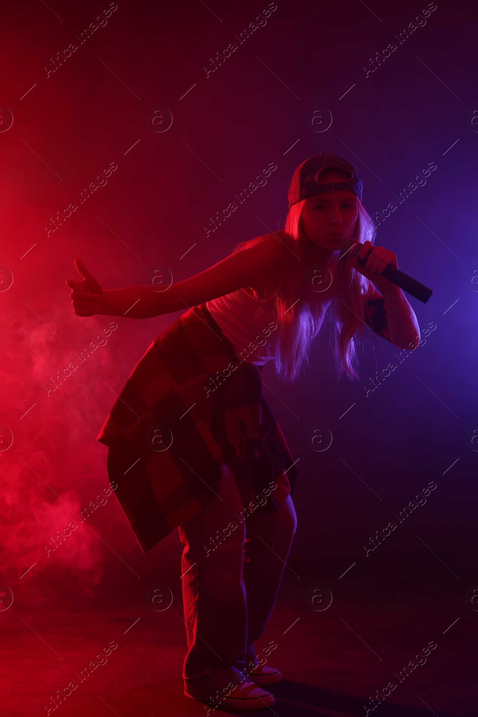 Photo of Talented singer performing on dark background with color lights and smoke