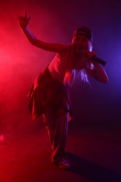 Photo of Talented singer performing on dark background with color lights and smoke