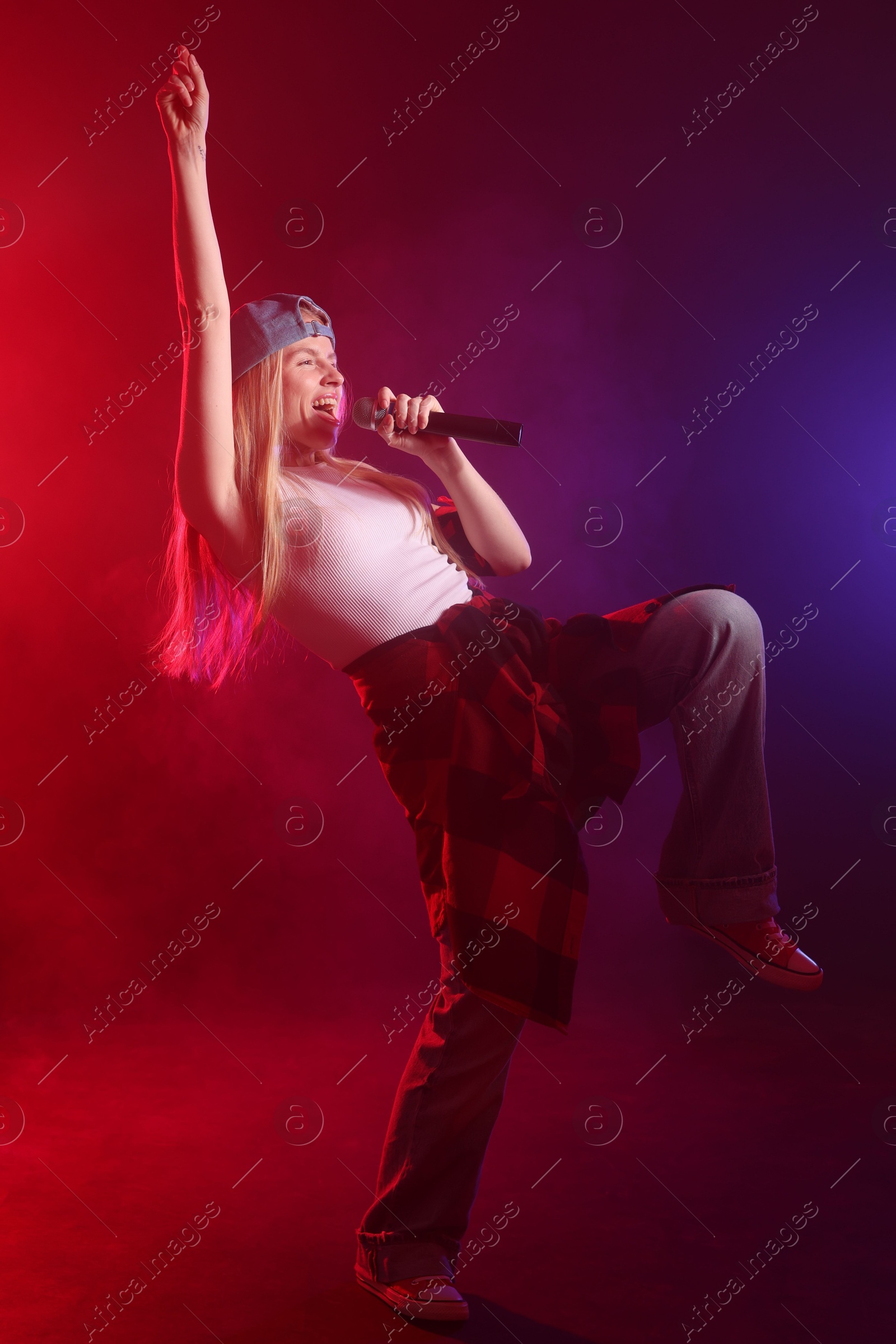 Photo of Talented singer performing on dark background with color lights and smoke