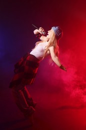 Photo of Talented singer performing on dark background with color lights and smoke