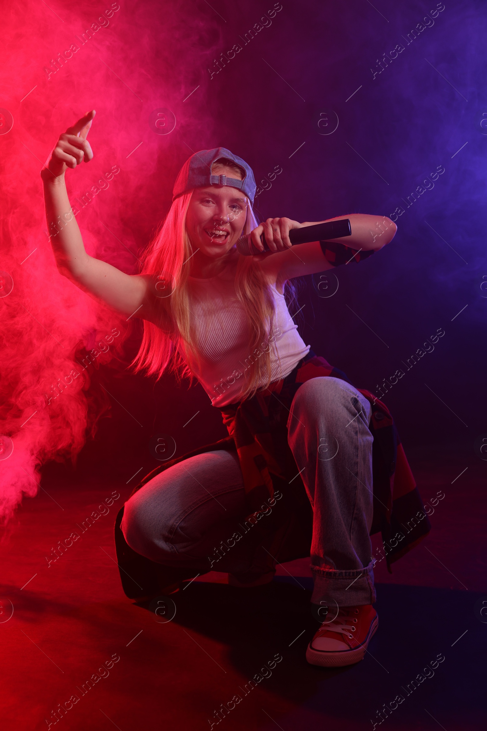 Photo of Talented singer performing on dark background with color lights and smoke