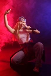 Photo of Talented singer performing on dark background with color lights and smoke