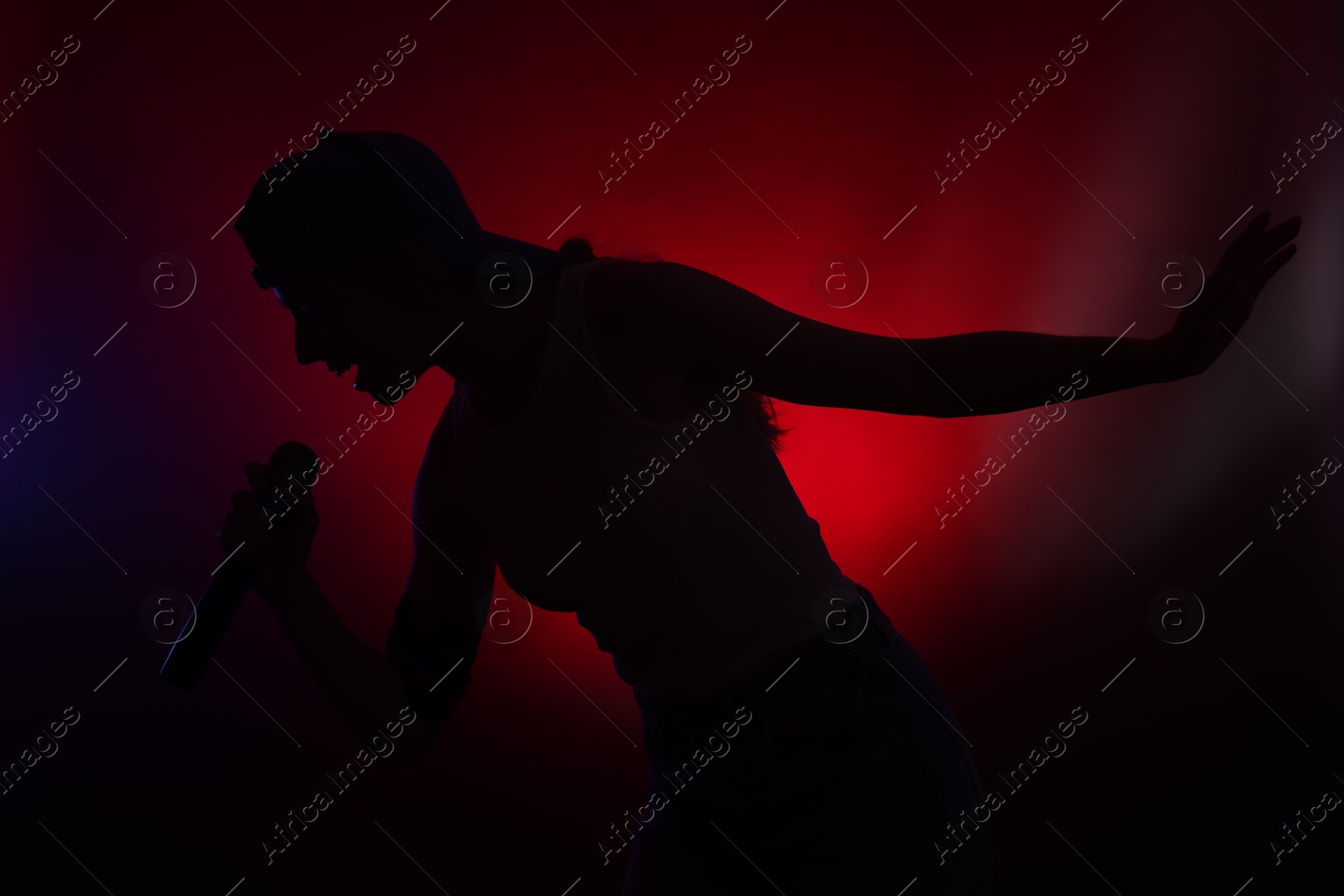 Photo of Silhouette of woman singing on dark background with color lights