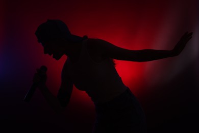 Photo of Silhouette of woman singing on dark background with color lights