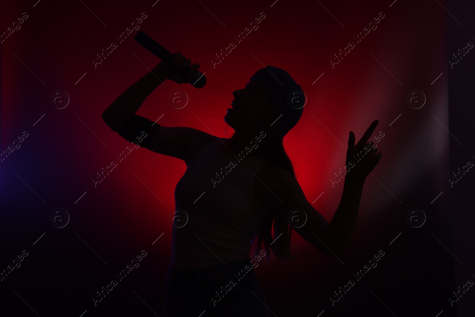 Photo of Silhouette of woman singing on dark background with color lights