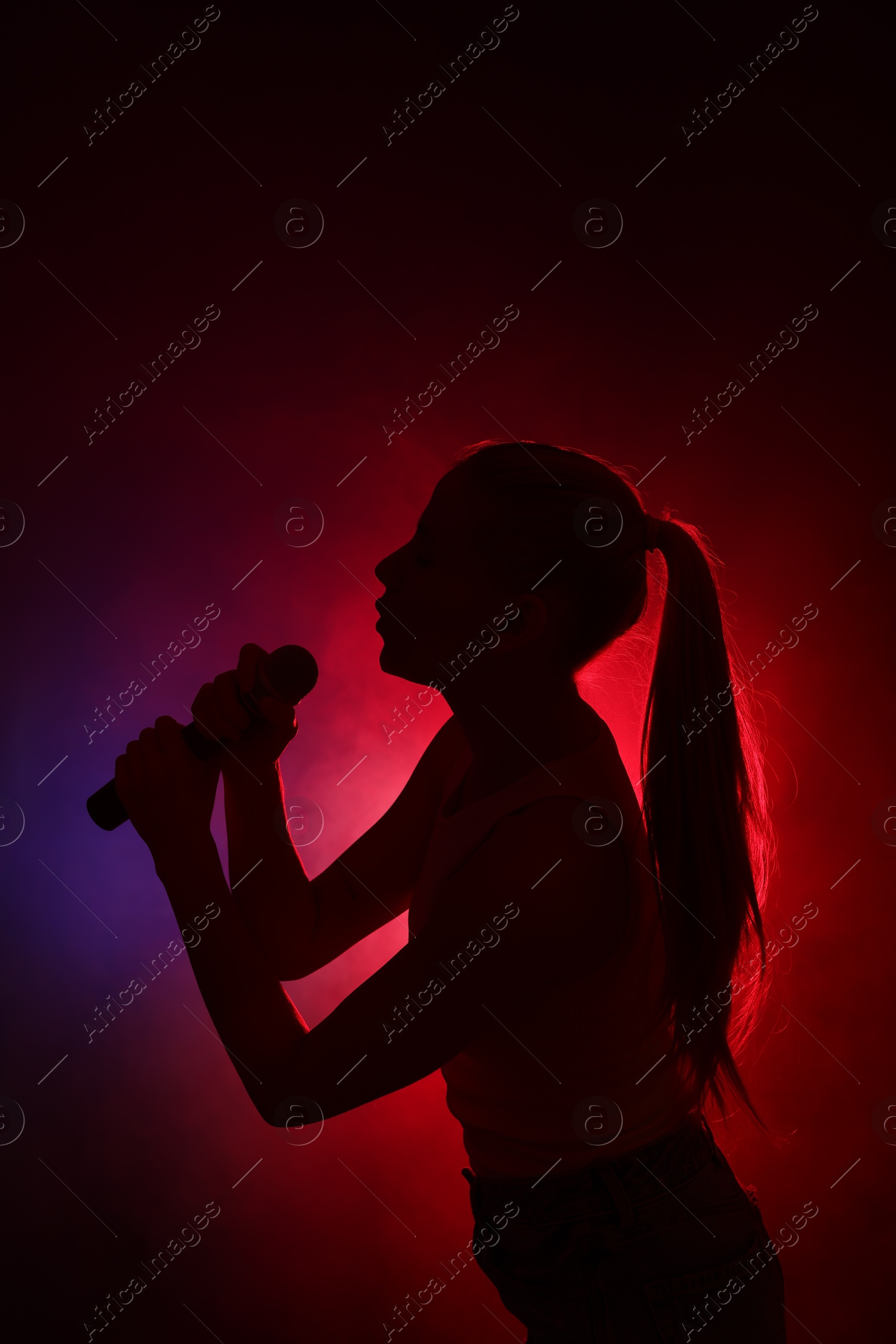 Photo of Silhouette of woman singing on dark background with color lights