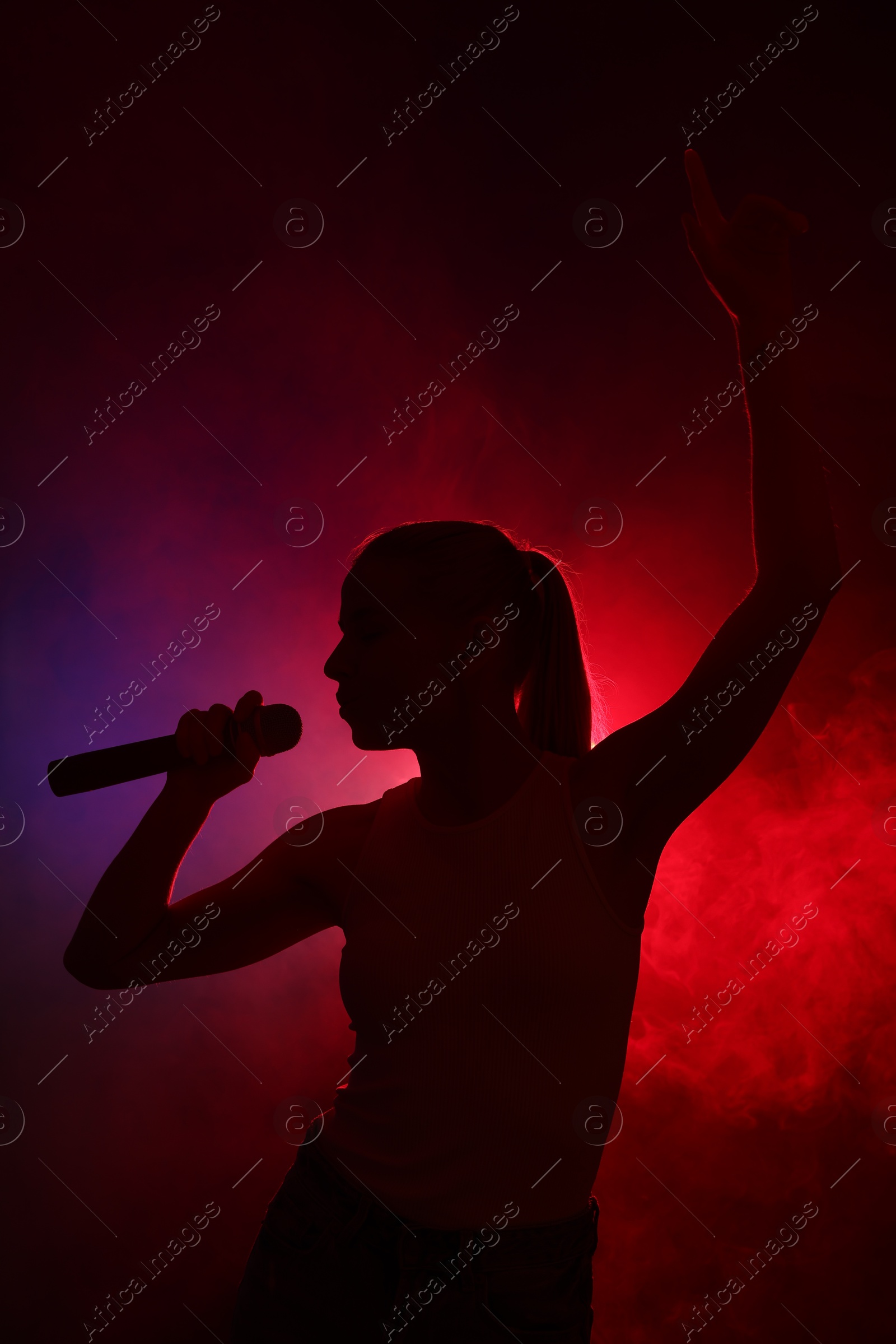 Photo of Silhouette of woman singing on dark background with color lights