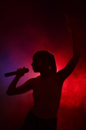 Silhouette of woman singing on dark background with color lights