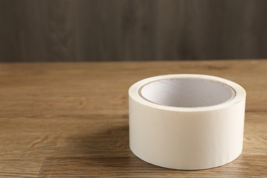 Roll of masking tape on wooden table, closeup. Space for text