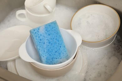 Photo of Blue sponge, dishes and foam in sink, closeup