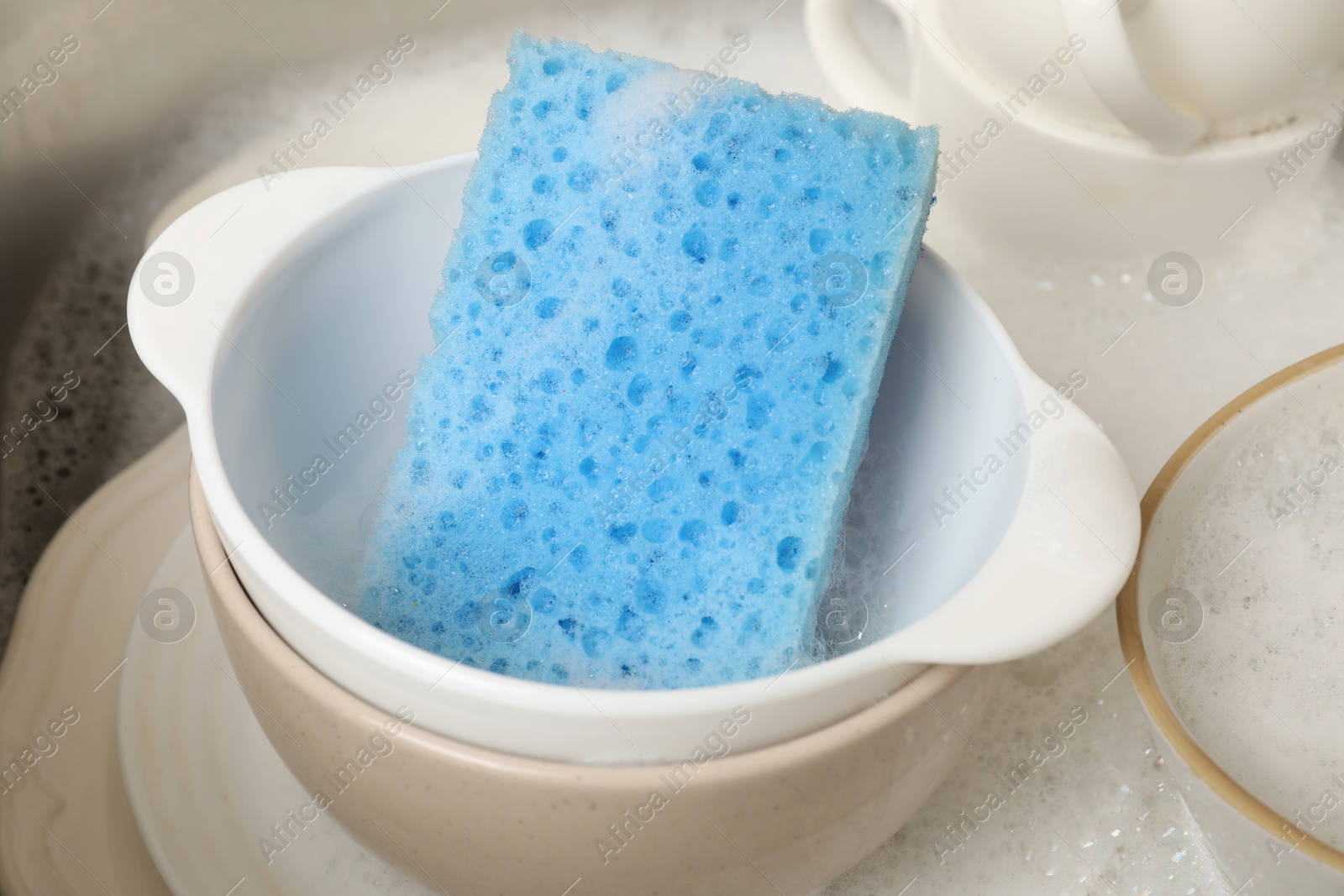 Photo of Blue sponge, dishes and foam in sink, closeup