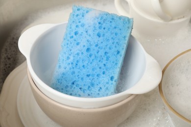 Photo of Blue sponge, dishes and foam in sink, closeup