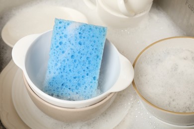 Photo of Blue sponge, dishes and foam in sink, closeup