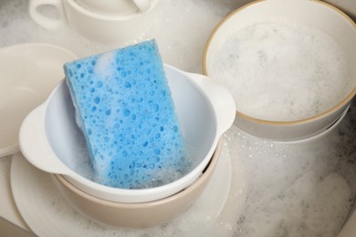 Photo of Blue sponge, dishes and foam in sink, closeup