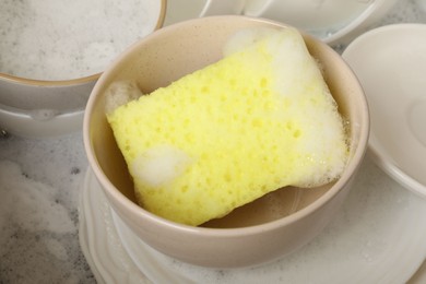 Photo of Yellow sponge, dishes and foam in sink, closeup