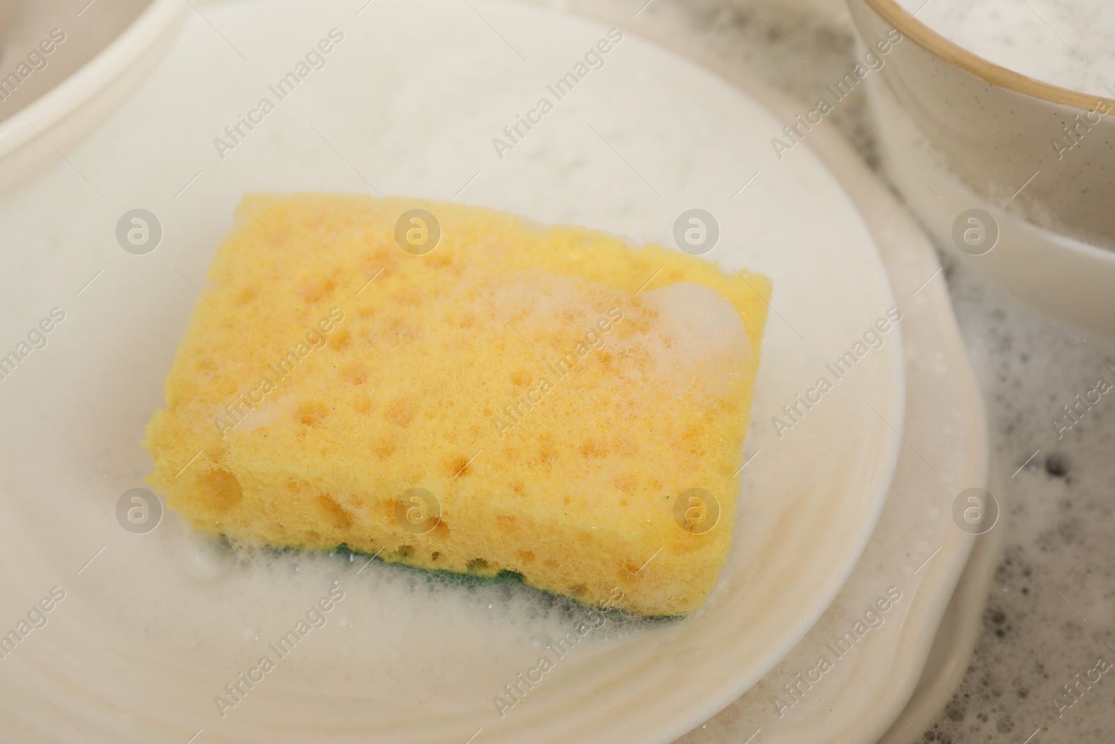 Photo of Yellow sponge, dishes and foam in sink, closeup