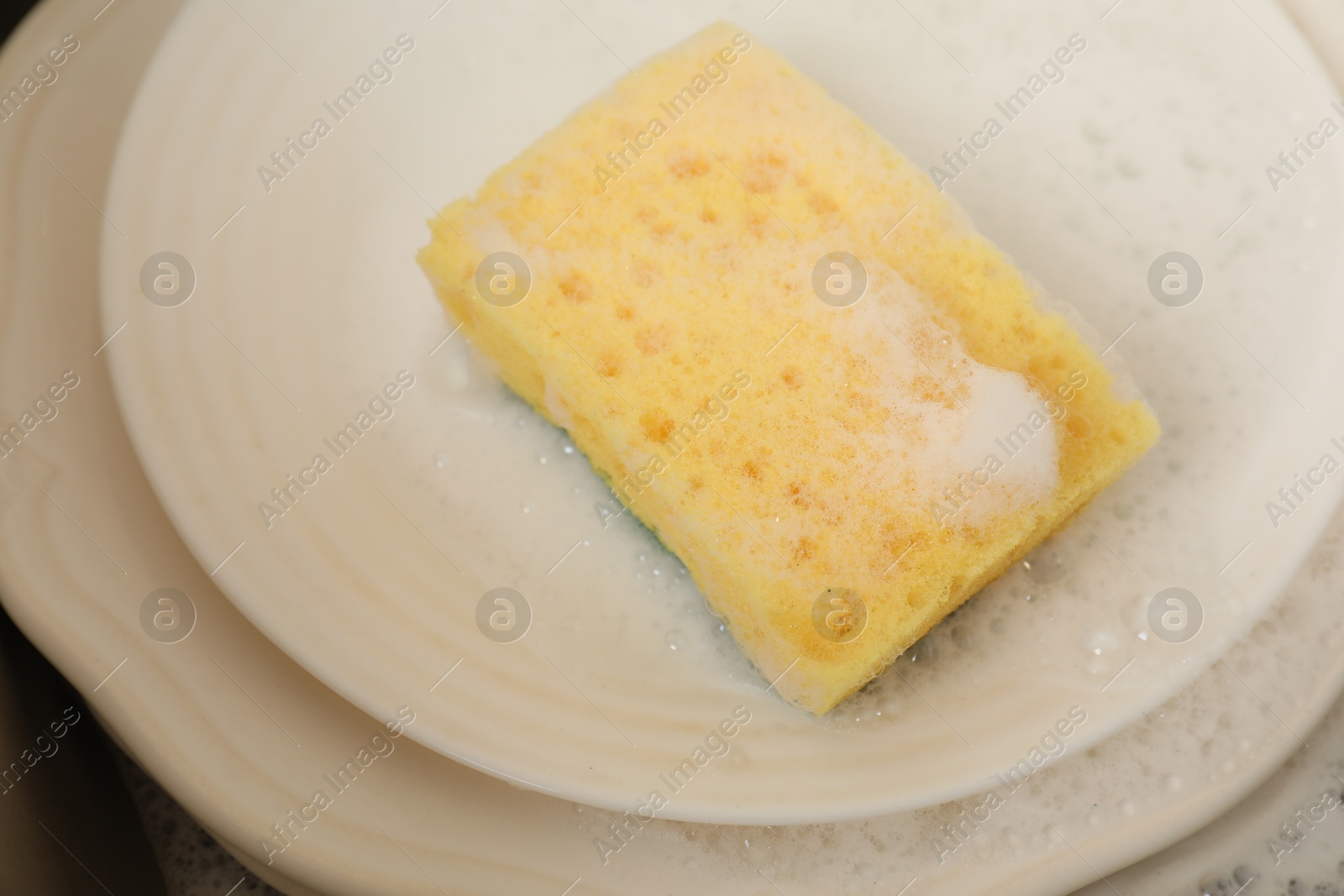 Photo of Yellow sponge, dishes and foam in sink, closeup