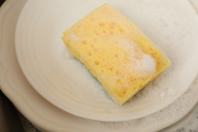 Photo of Yellow sponge, dishes and foam in sink, closeup