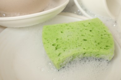 Photo of Green sponge, dishes and foam in sink, closeup