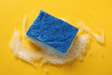 Photo of One cleaning sponge and foam on yellow background, above view