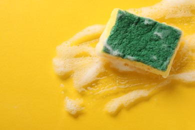 Photo of One cleaning sponge and foam on yellow background, top view. Space for text