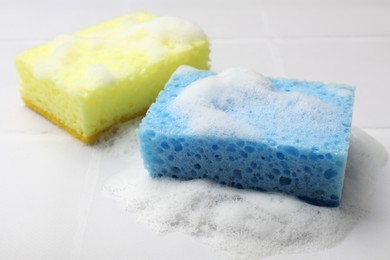 Photo of Sponges and foam on white tiled table, closeup