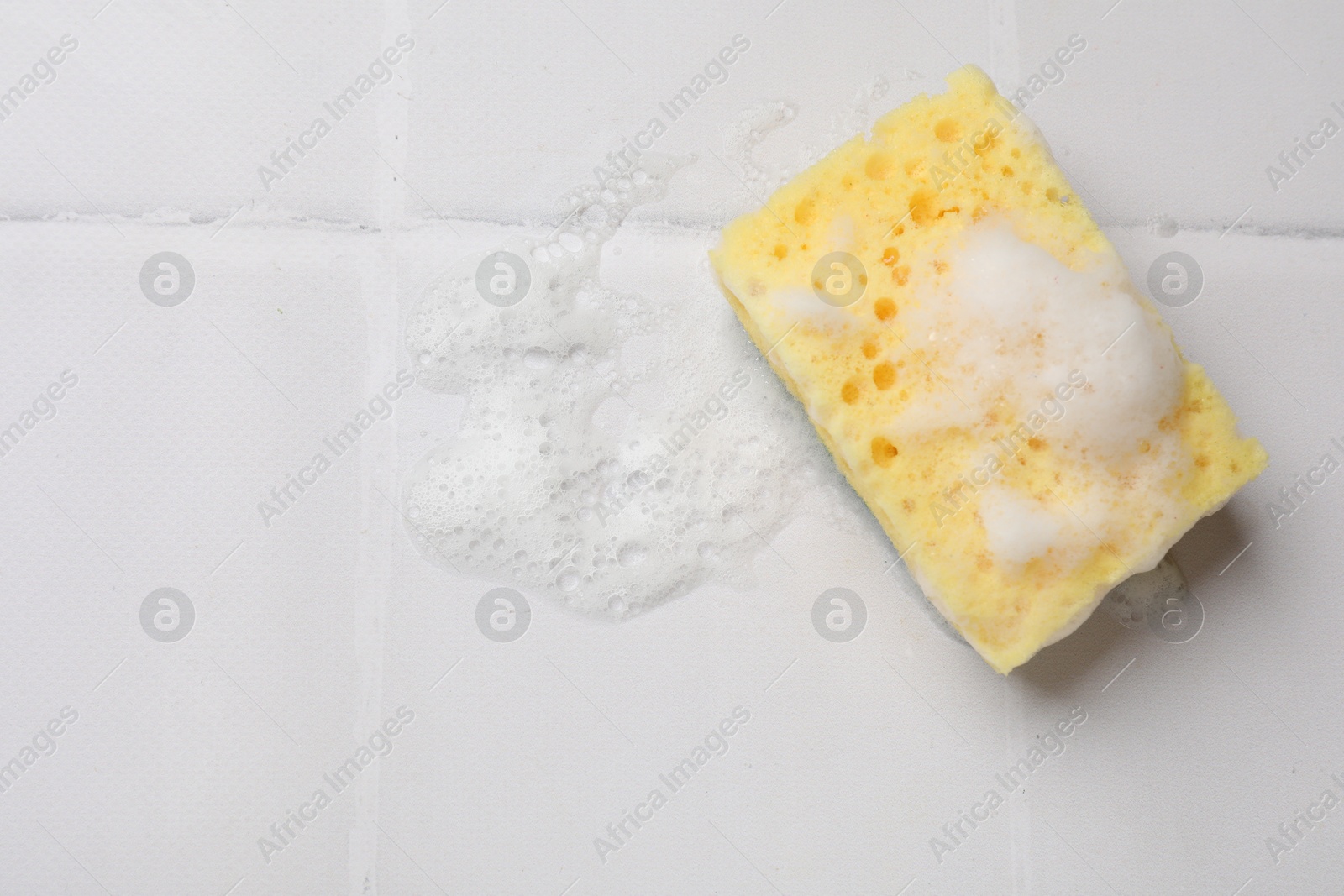 Photo of Sponge and foam on white tiled table, top view. Space for text