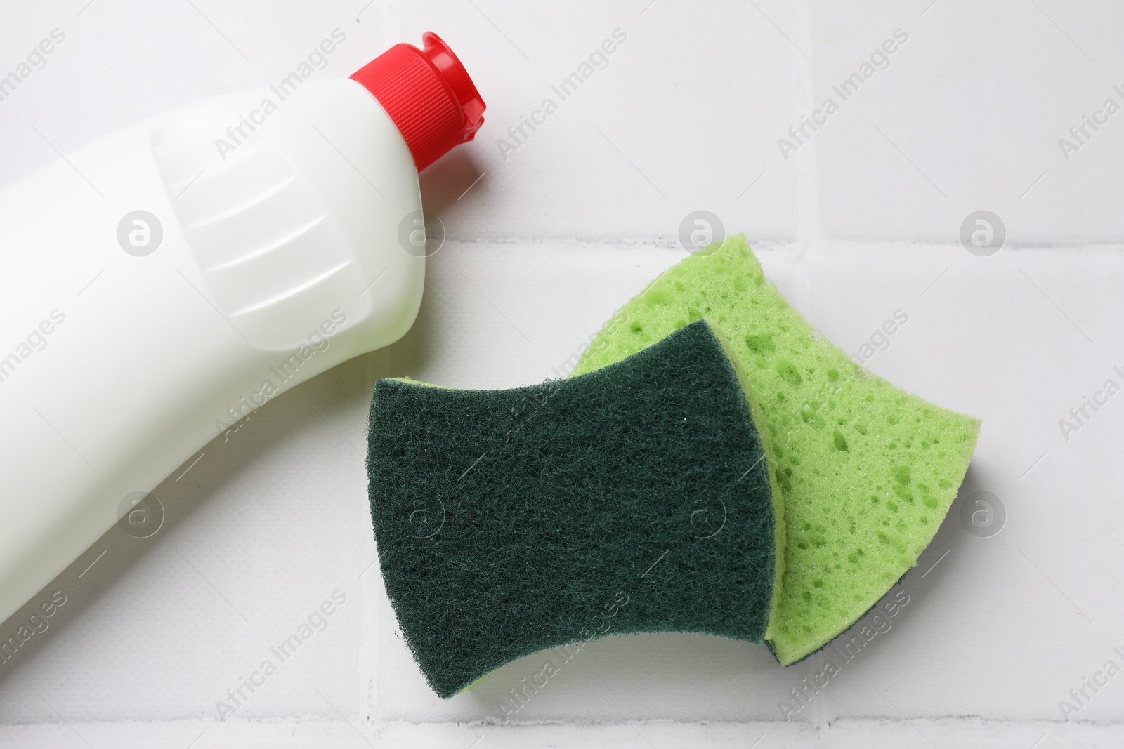 Photo of Sponges and bottle of dish soap on white tiled table, flat lay