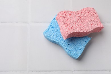 Photo of Soft sponges on white tiled table, top view. Space for text