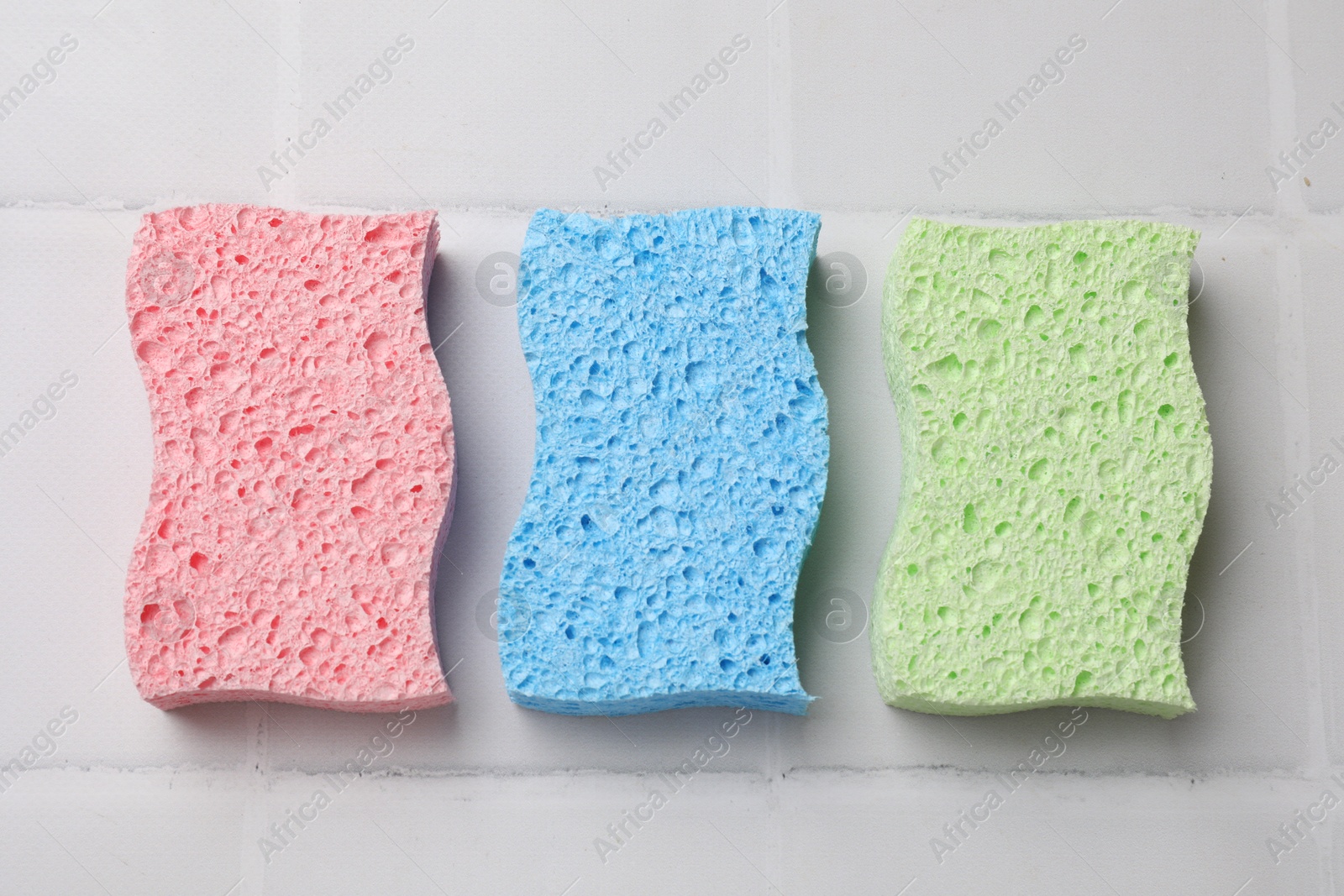 Photo of Soft sponges on white tiled table, flat lay