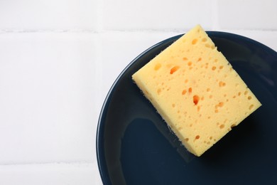 Photo of Sponge and plate on white tiled table, top view. Space for text