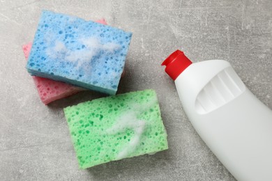 Photo of Sponges, foam and dish soap on light grey table, flat lay