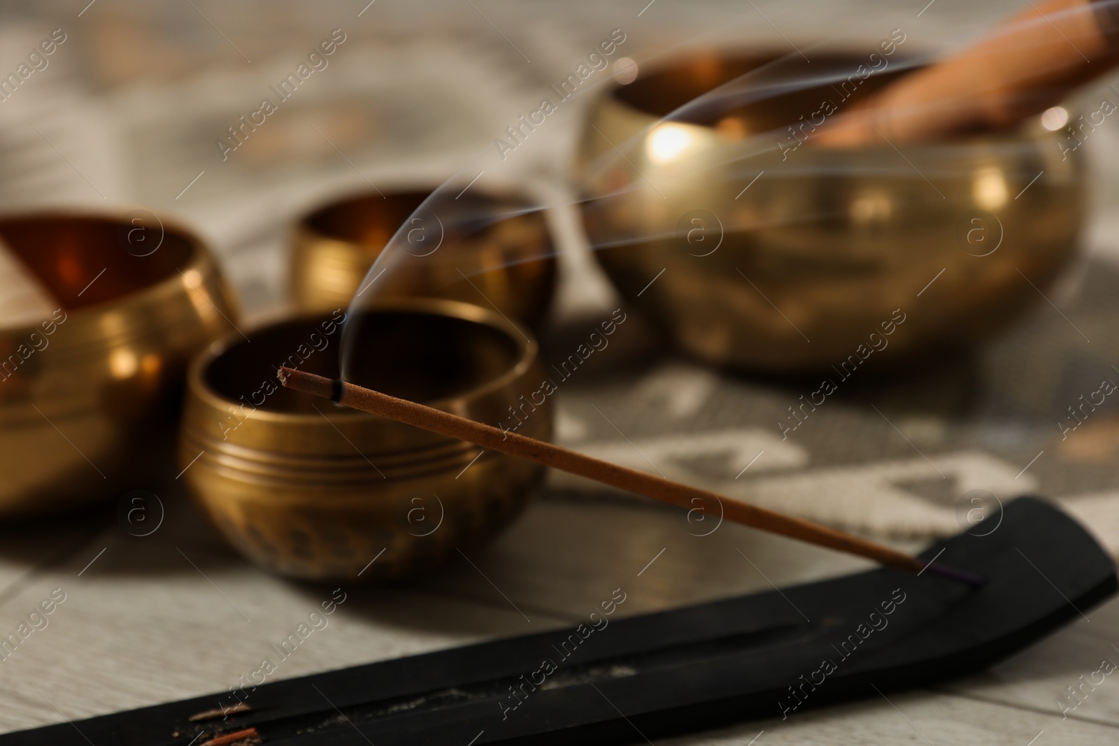 Photo of Incense stick smoldering in holder and tibetan singing bowls on floor, closeup