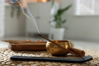 Photo of Incense stick smoldering in holder and tibetan singing bowl on wicker mat indoors