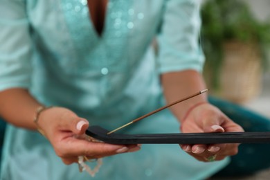 Photo of Young woman with incense stick smoldering in holder indoors, closeup