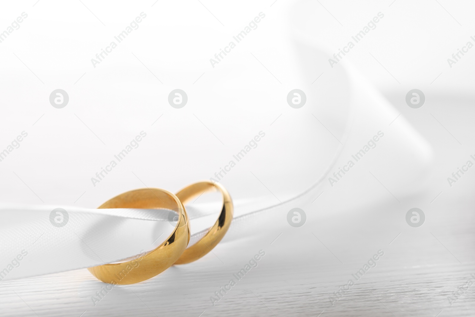 Photo of Beautiful golden wedding rings and white ribbon on light wooden background