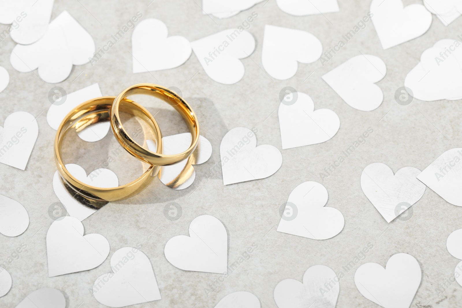 Photo of Beautiful golden wedding rings and heart shaped confetti on gray background, above view