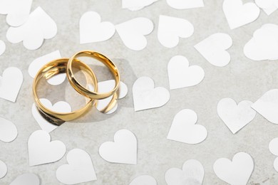 Photo of Beautiful golden wedding rings and heart shaped confetti on gray background, above view