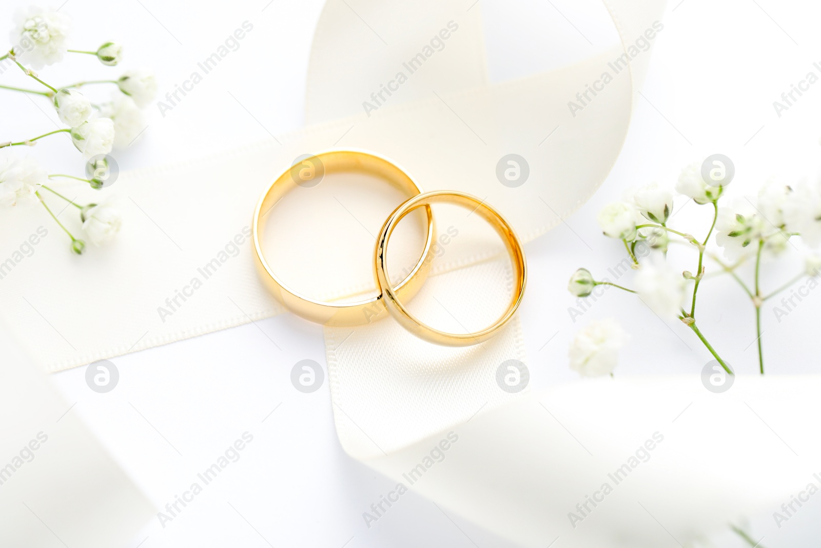 Photo of Golden wedding rings, ribbon and flowers on white background