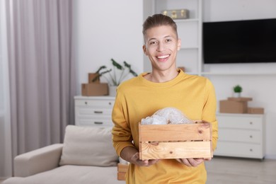 Photo of Happy man holding wooden crate with stuff in new apartment. Housewarming party