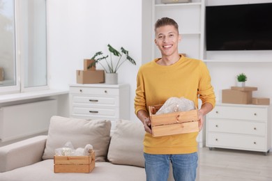 Happy man holding wooden crate with stuff in new apartment. Housewarming party