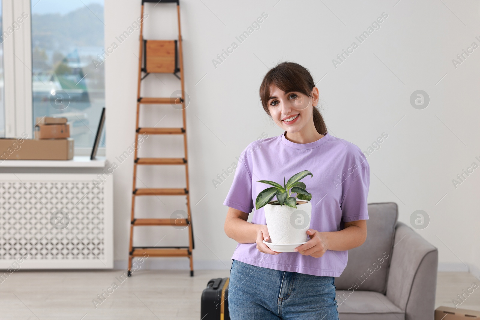 Photo of Happy woman with houseplant in new apartment. Housewarming party