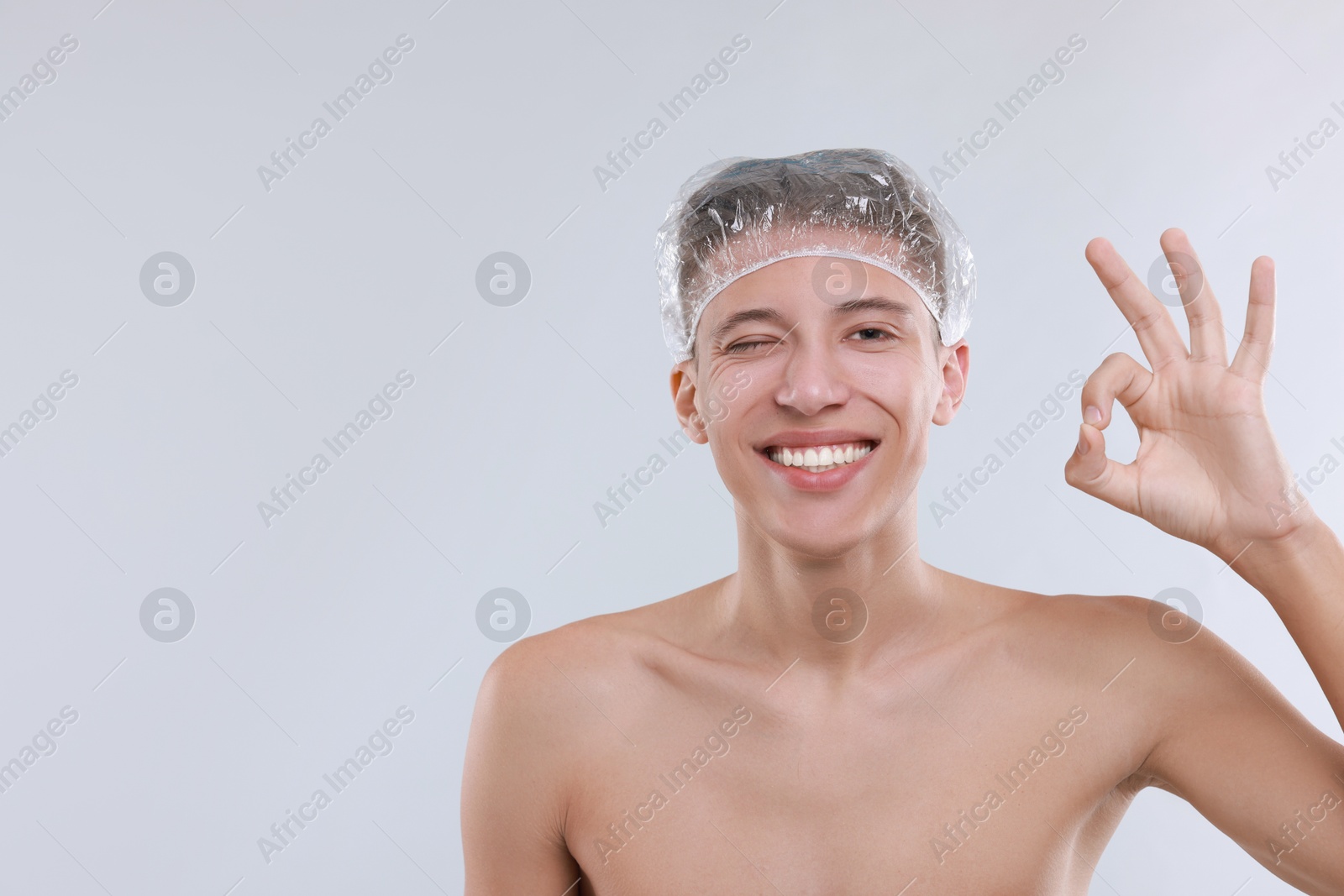 Photo of Man in shower cap showing ok gesture on light grey background, space for text