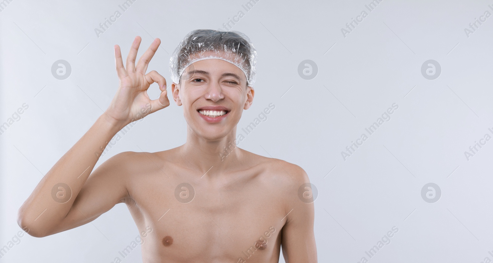 Photo of Man in shower cap showing ok gesture on light grey background, space for text